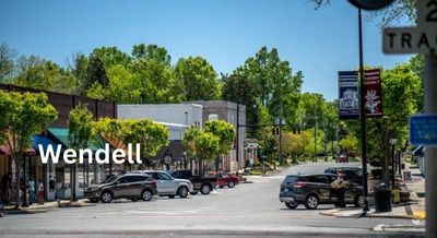 A quaint downtown Wendell, NC, scene with small shops, parked cars, leafy trees, and a clear blue sky.