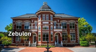 Historic building in Zebulon, NC, with red brick facade, arched windows, and lush greenery against a bright blue sky.